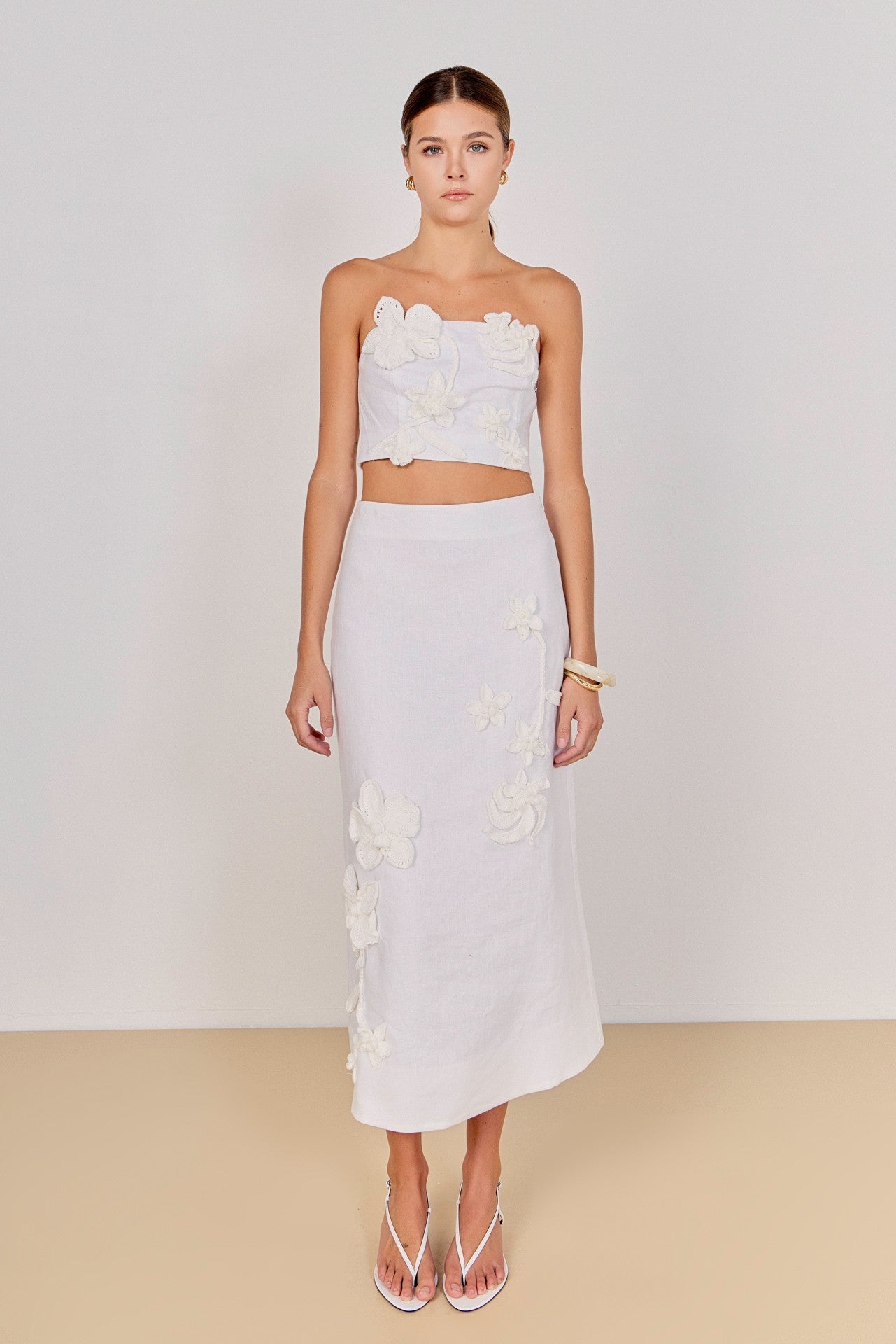 Woman wearing a white floral top and skirt set against a plain background