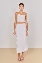 Woman wearing a white floral top and skirt set against a plain background