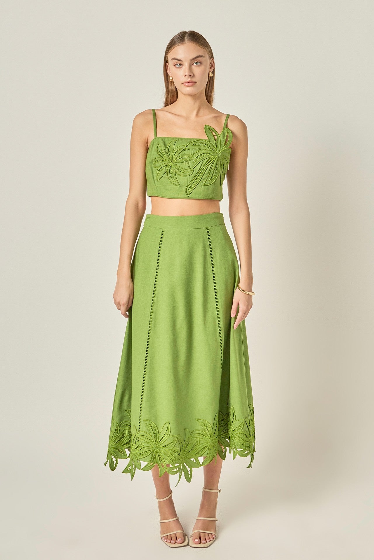 Woman wearing a green two-piece outfit with lace details on a plain background