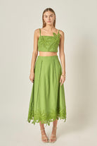 Woman wearing a green two-piece outfit with lace details on a plain background