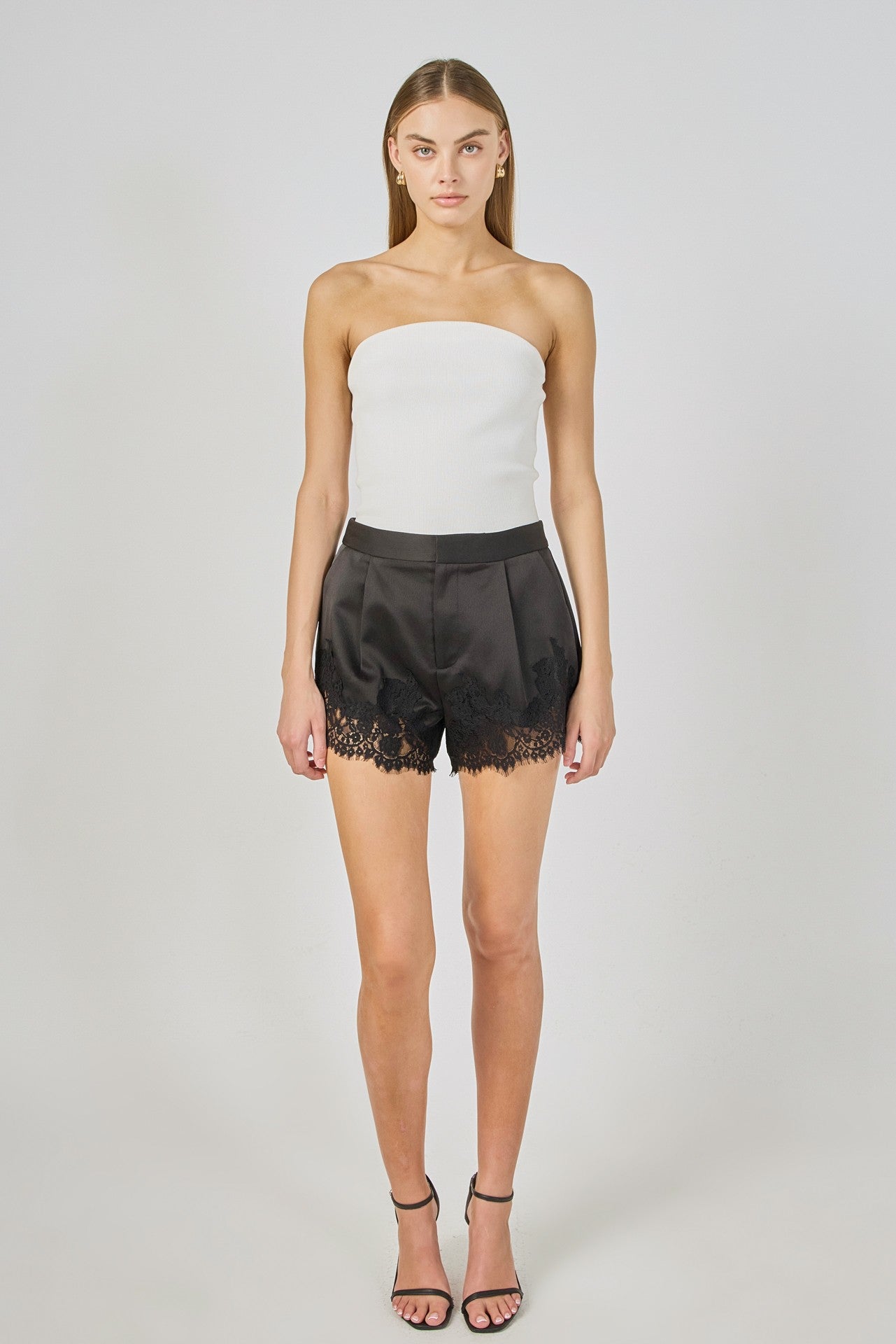 Woman wearing a white strapless top and black lace shorts on a plain background