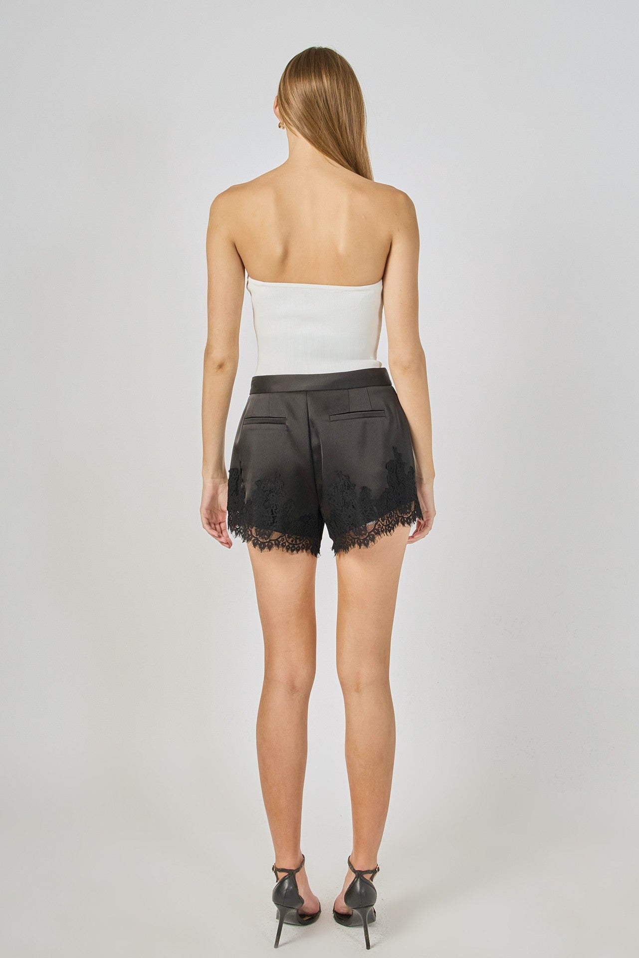 Person wearing a white strapless top and black lace shorts on a plain background