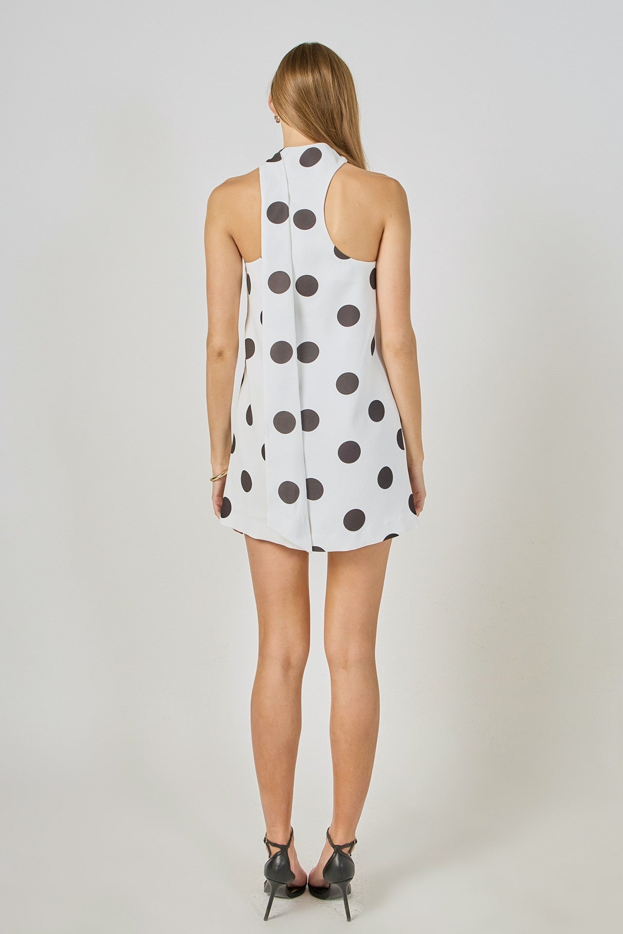 Woman wearing a white dress with black polka dots from behind on a plain background