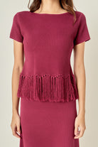 A woman wearing a textured short-sleeve top in a deep berry pink, featuring a fringed hem and a matching textured skirt against a light beige background.