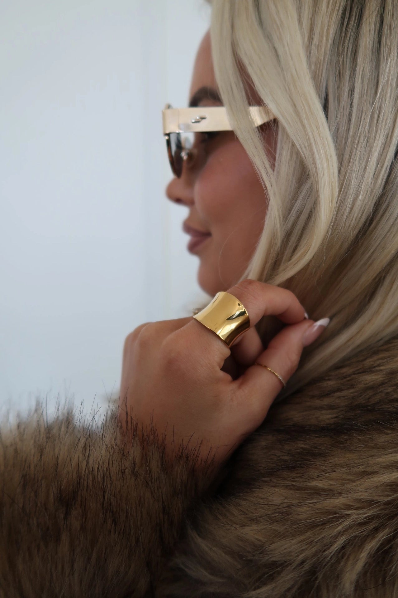 Person wearing a gold ring and sunglasses with a fur coat
