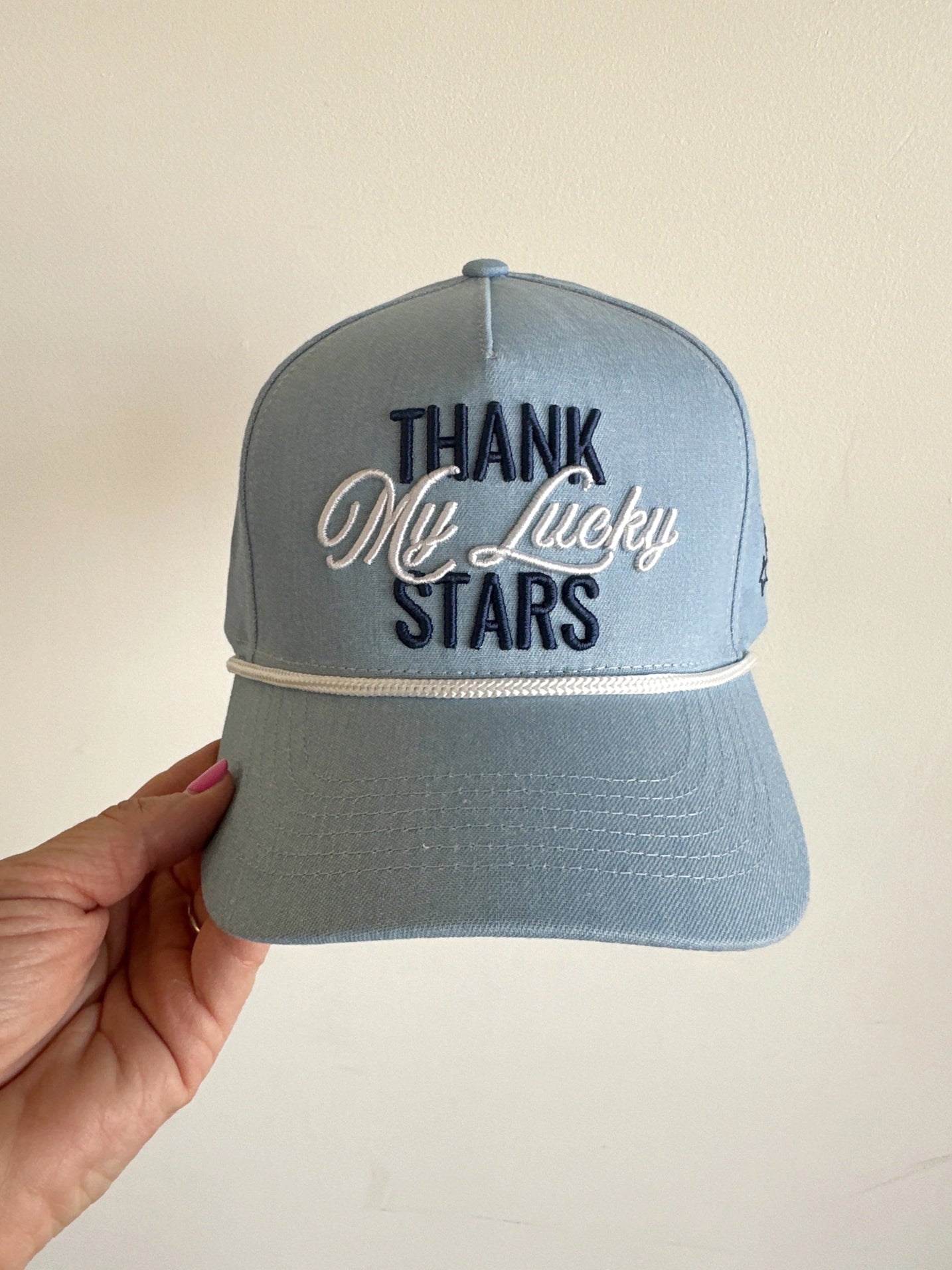 Blue cap with 'Thank my lucky stars' text held by a hand on a beige background