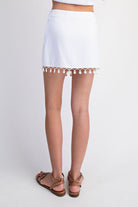 White skirt with tassel trim worn by a person on a white background