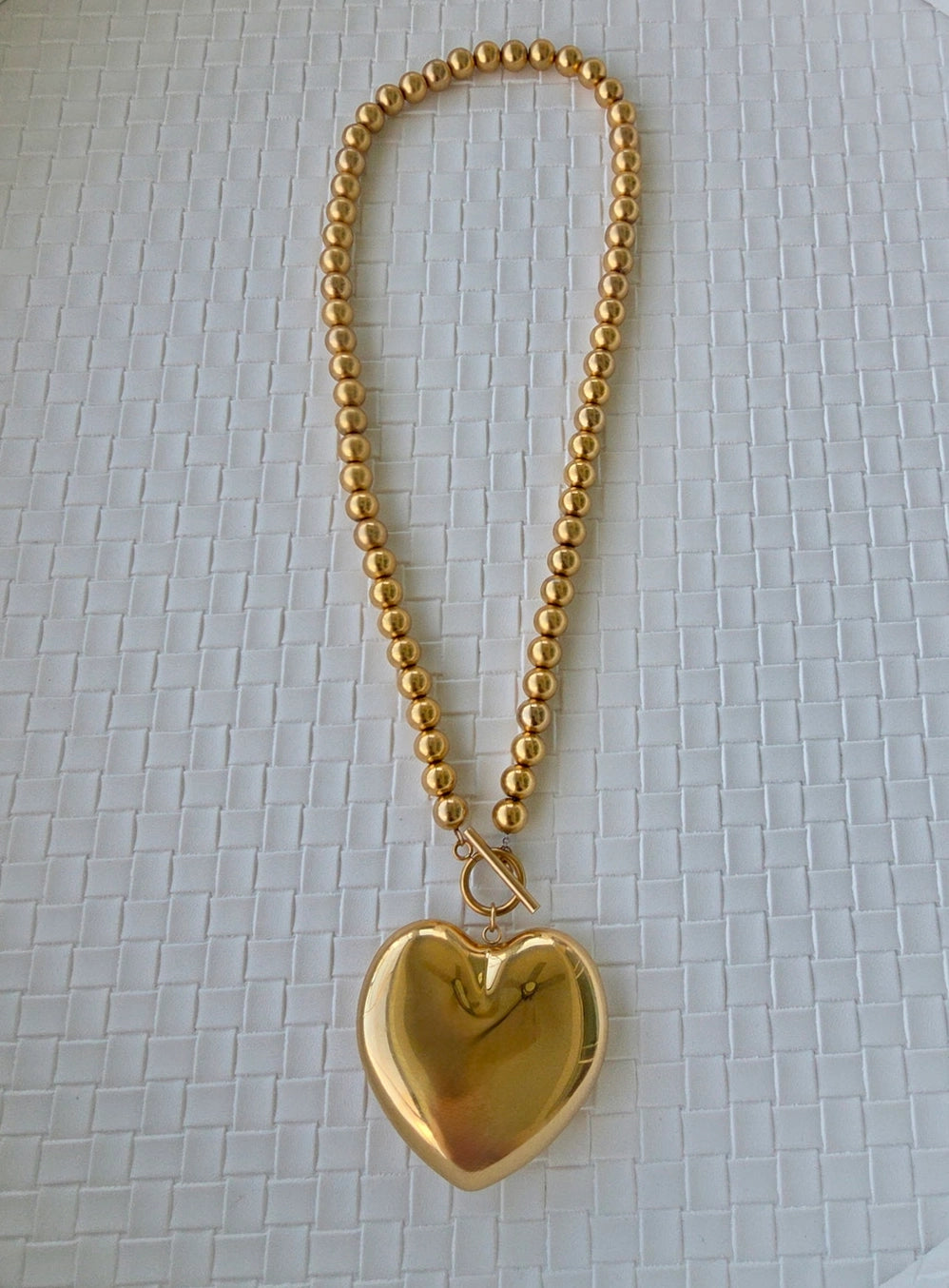 Gold heart-shaped pendant on a chain against a textured white background