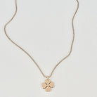 A delicate gold chain necklace with a small four-petal flower pendant, displayed on a clean white background.