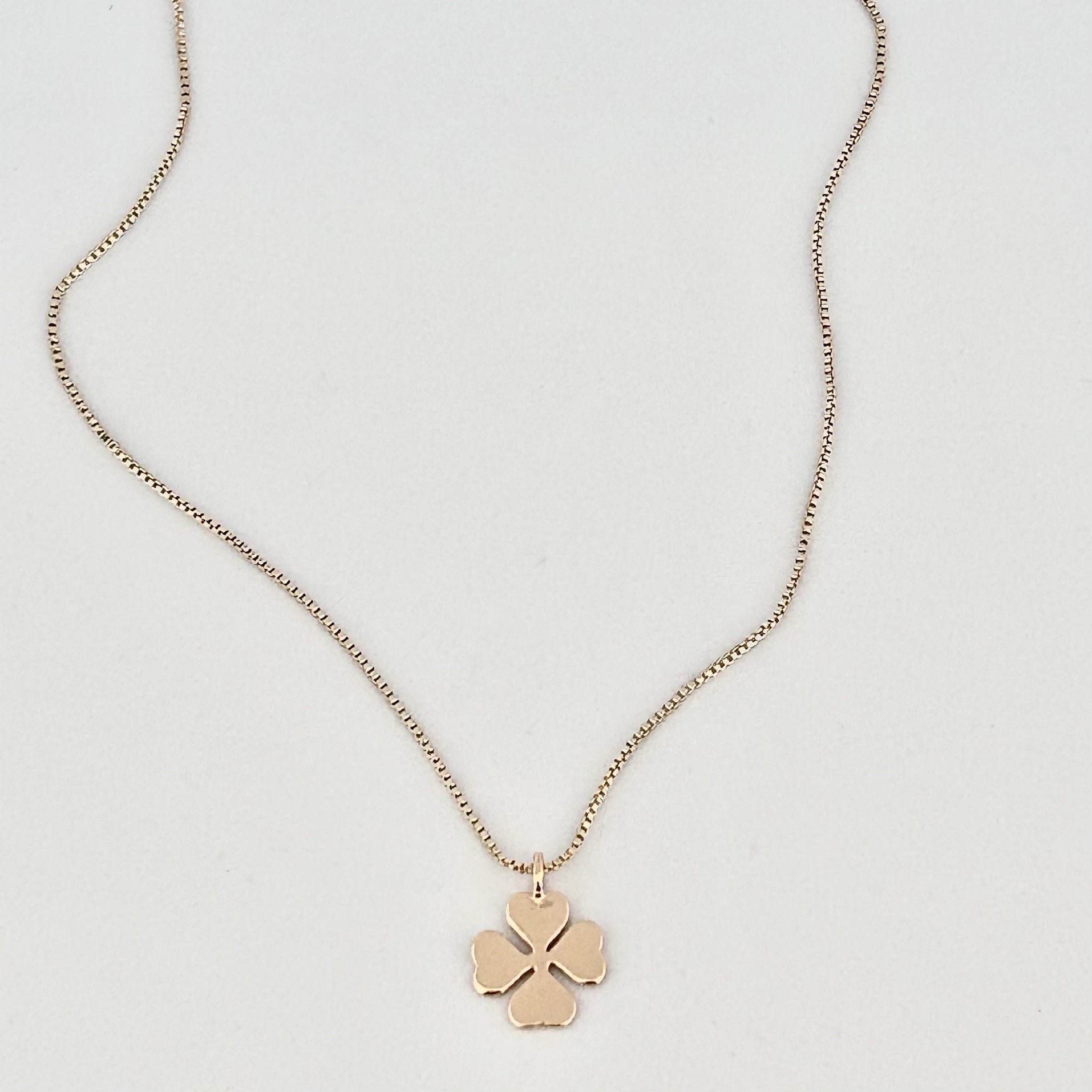 A delicate gold chain necklace with a small four-petal flower pendant, displayed on a clean white background.