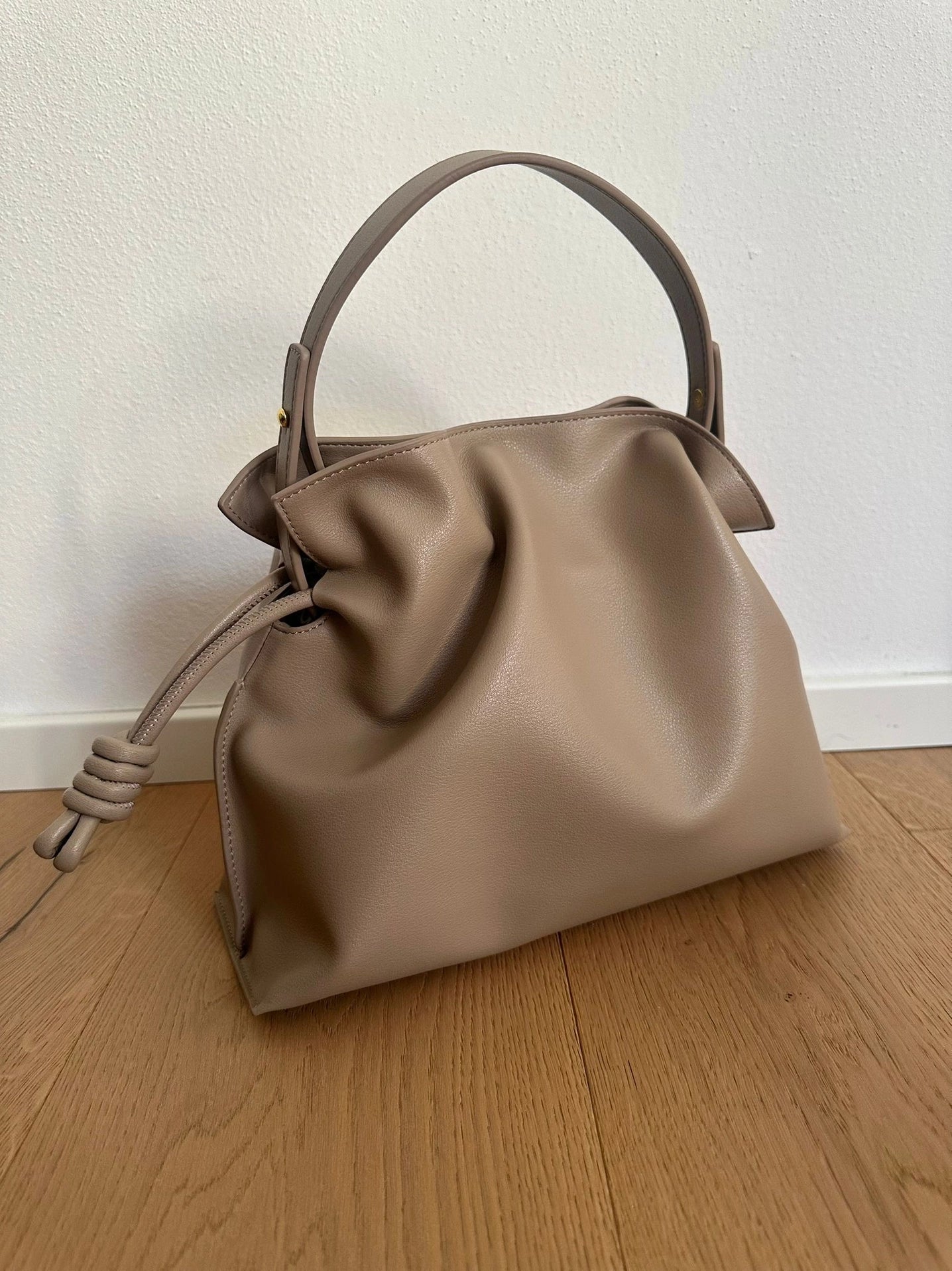 Beige real leather handbag on a wooden floor with a white wall background