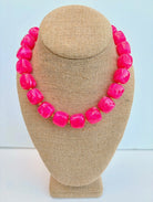 Necklace with bright pink beads on a beige mannequin bust against a light blue background