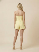 Woman wearing a yellow strapless romper against a beige background