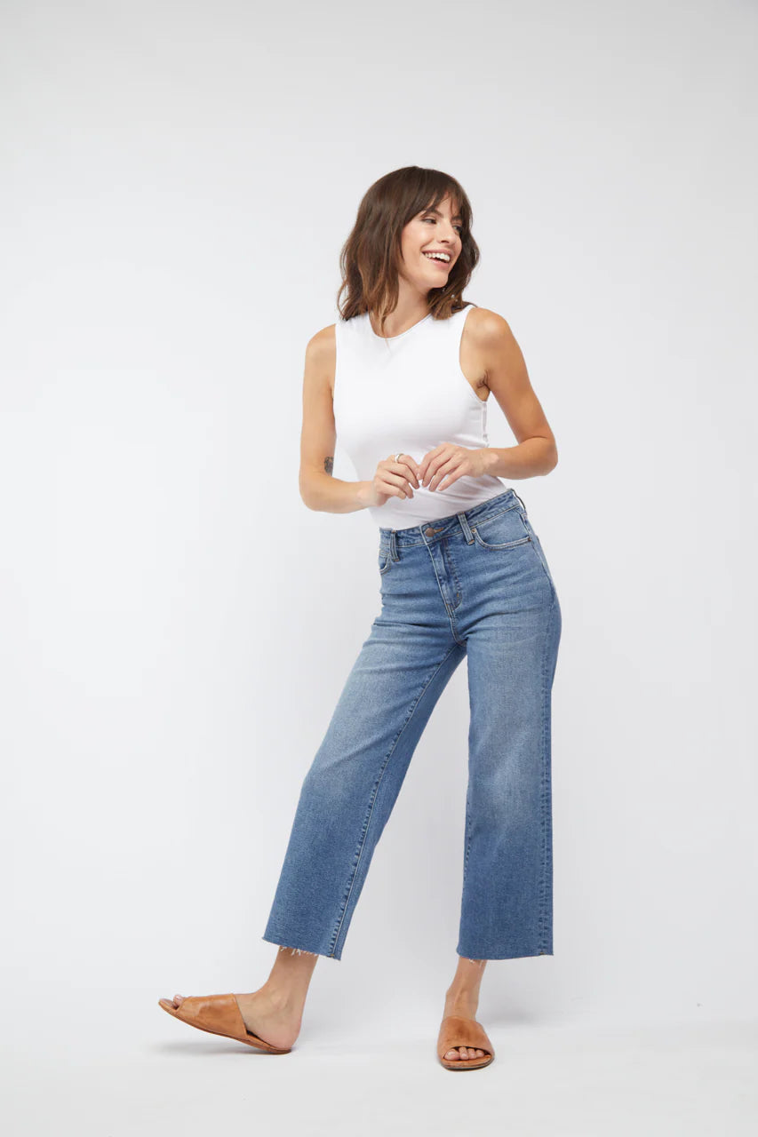 Woman wearing a white sleeveless top and blue jeans on a white background