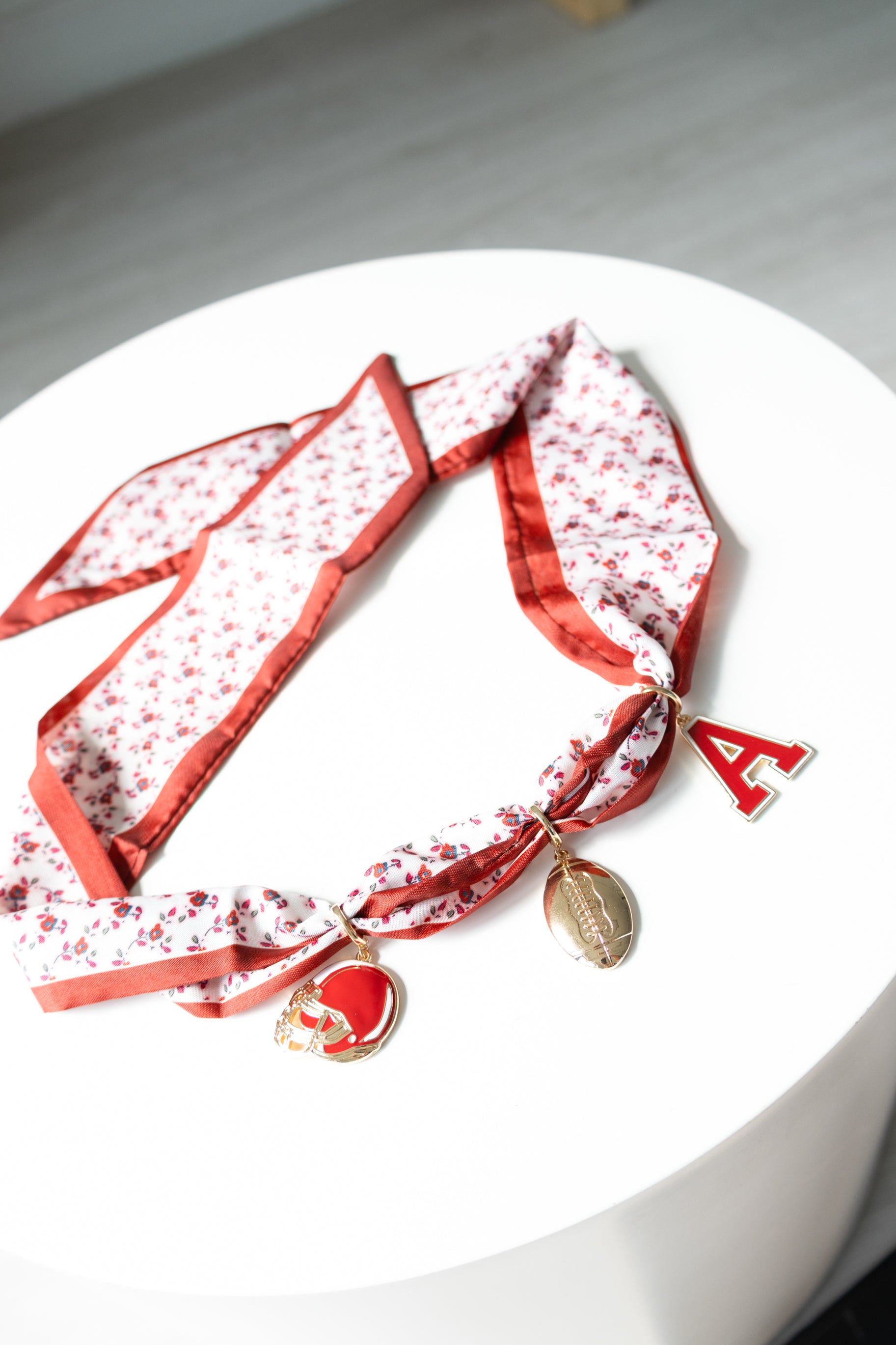 Red floral-patterned scarf with gold charms on a white surface