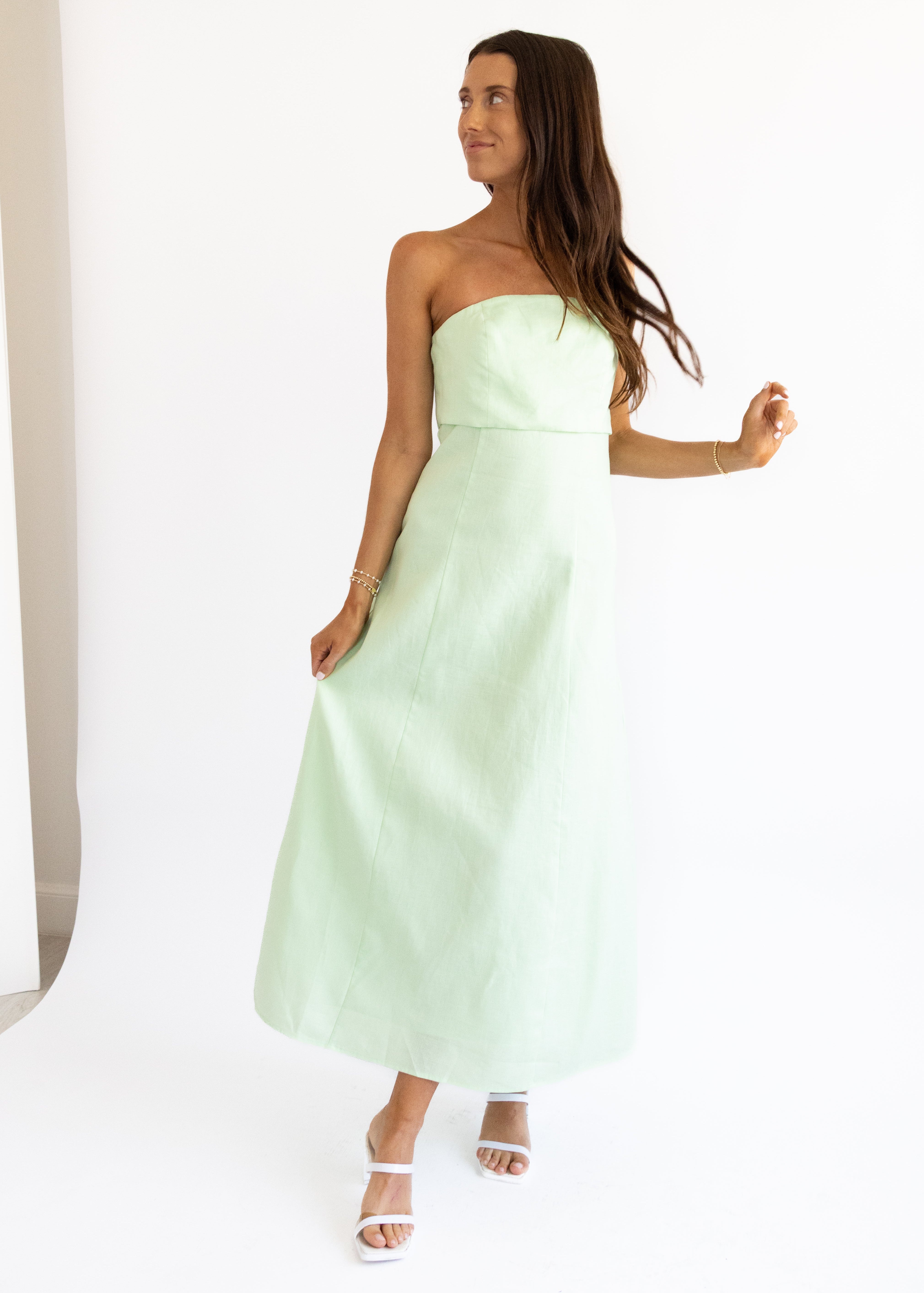 A woman wearing a strapless maxi dress in a pistachio green color with a fold over front panel, standing in a relaxed pose.