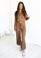 Woman wearing a brown tracksuit with white piping on a white background
