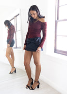 Woman wearing a red off-shoulder top and black skirt in a white room.