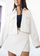 Woman wearing a white jacket and skirt set with a black top on a white background