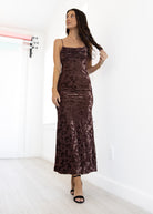 Woman wearing a brown floral velvet dress in a minimal white room