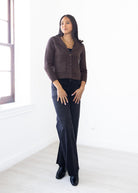 Woman wearing a brown jacket and dark jeans standing in a bright room.