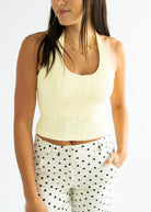Woman wearing a light yellow sleeveless top and polka dot pants on a white background