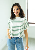 Woman wearing a green and white striped shirt and blue jeans indoors.