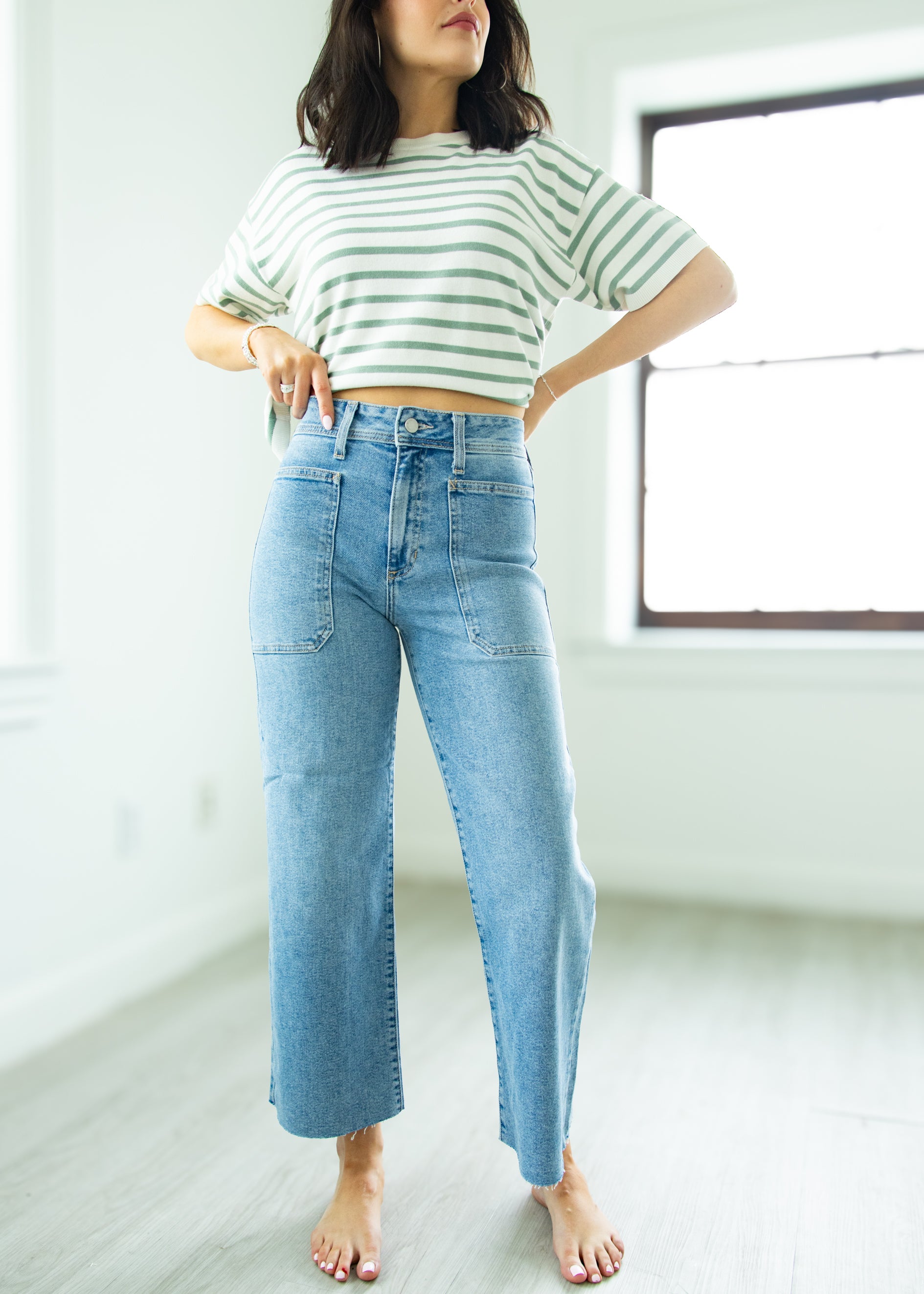 Person wearing a striped shirt and blue jeans in a minimalistic room.