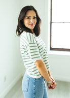 Woman wearing a green and white striped shirt and blue jeans indoors.
