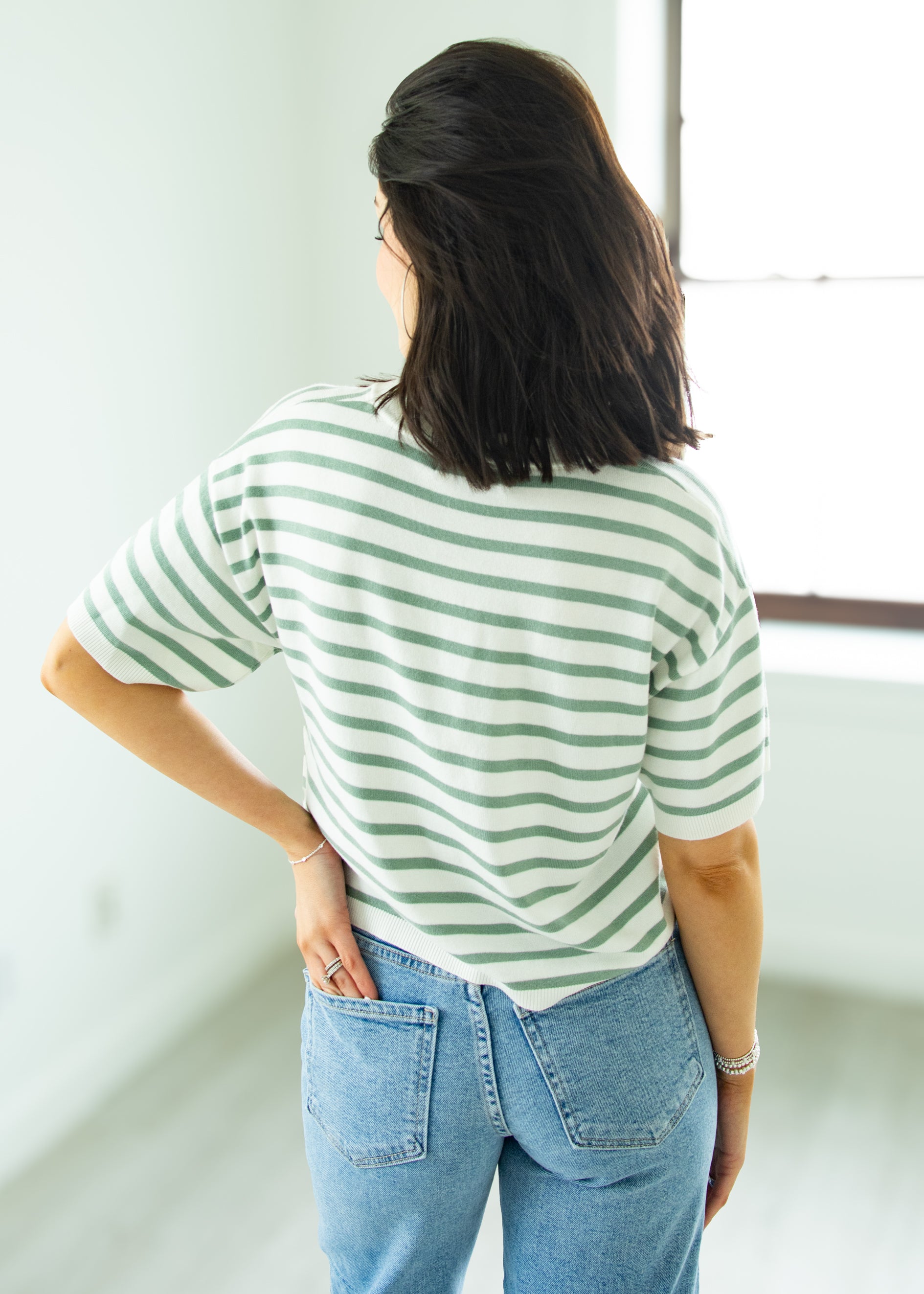 Person wearing a green and white striped shirt and blue jeans in a minimal indoor setting.
