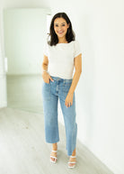 Woman wearing a white t-shirt and blue jeans standing in a minimalistic room.