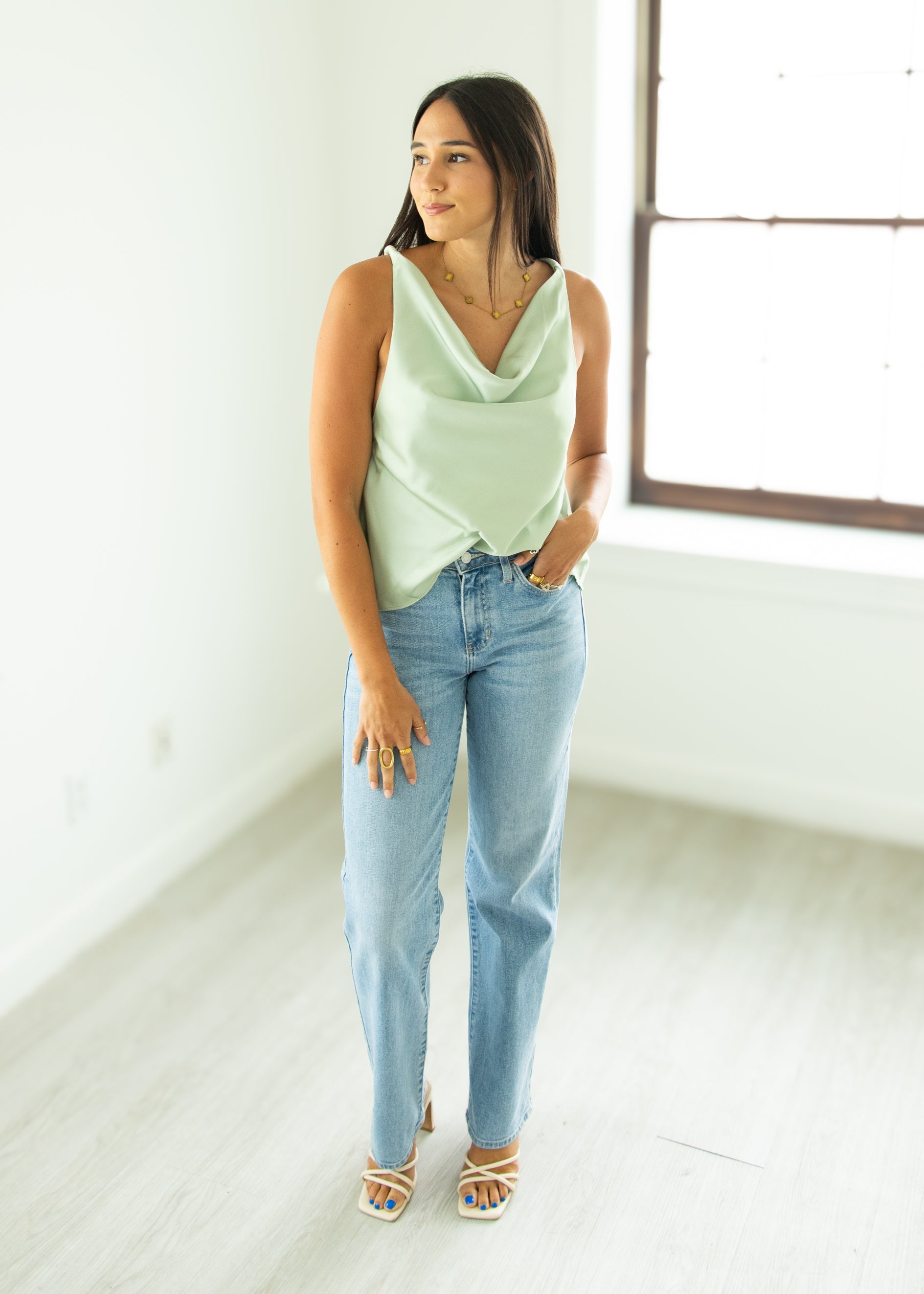 Woman wearing a light green sleeveless top and blue jeans in a bright room.