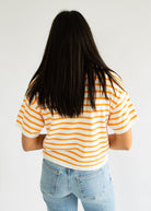 Person wearing a yellow and white striped shirt with blue jeans on a plain background
