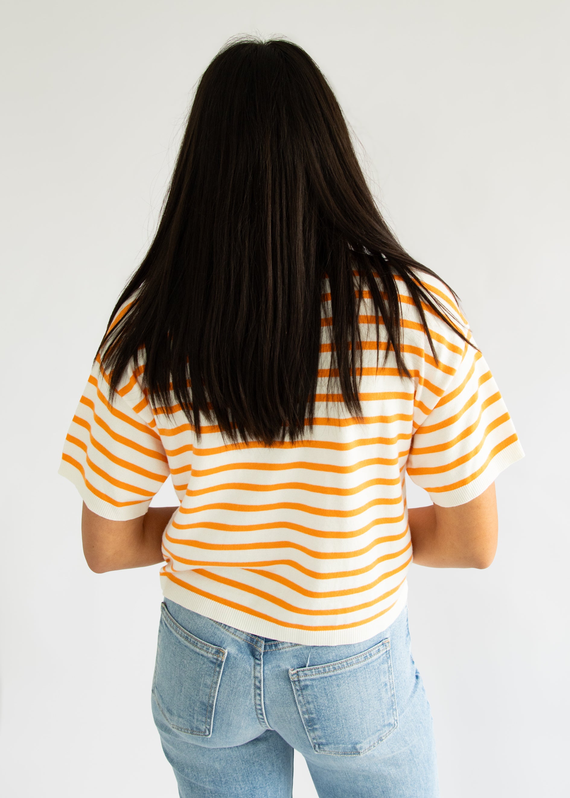 Person wearing a yellow and white striped shirt with blue jeans on a plain background