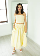 Woman wearing a yellow outfit standing in a bright room with large windows.