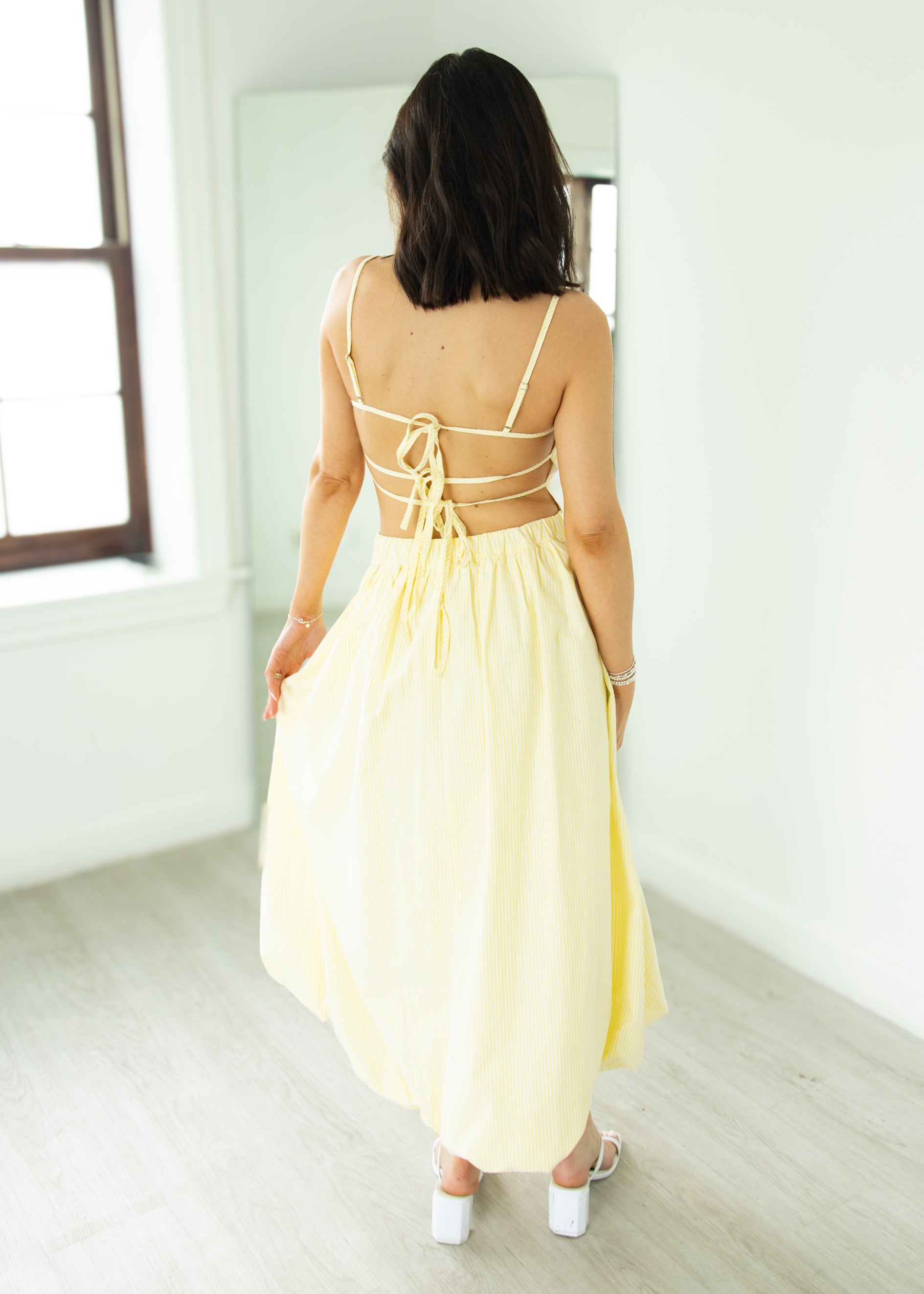 Woman wearing a yellow dress with a backless design in a minimal indoor setting.