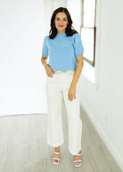 Woman wearing a light blue top and white pants in a minimalistic room.