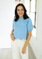 Woman wearing a light blue top with a yellow trim in an indoor setting