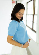 Woman wearing a light blue blouse and white pants indoors