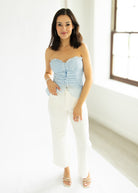 Woman wearing a light blue strapless top and white pants in a bright room.