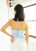 Woman wearing a light blue strapless top and white pants in an indoor setting.