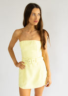 Woman wearing a light yellow strapless dress against a plain background