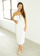 Woman in a white strapless dress with gold accents standing in a bright room.