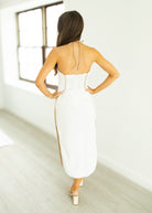 Woman in a white dress with gold accents standing in a minimalistic room.