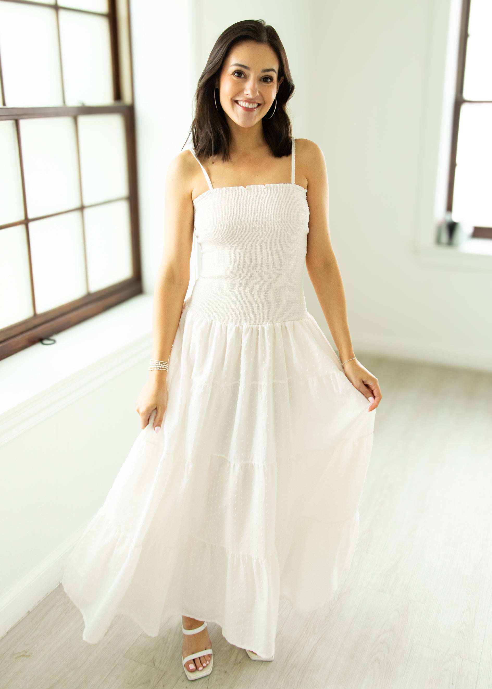 Woman wearing a white dress in a bright room with large windows.