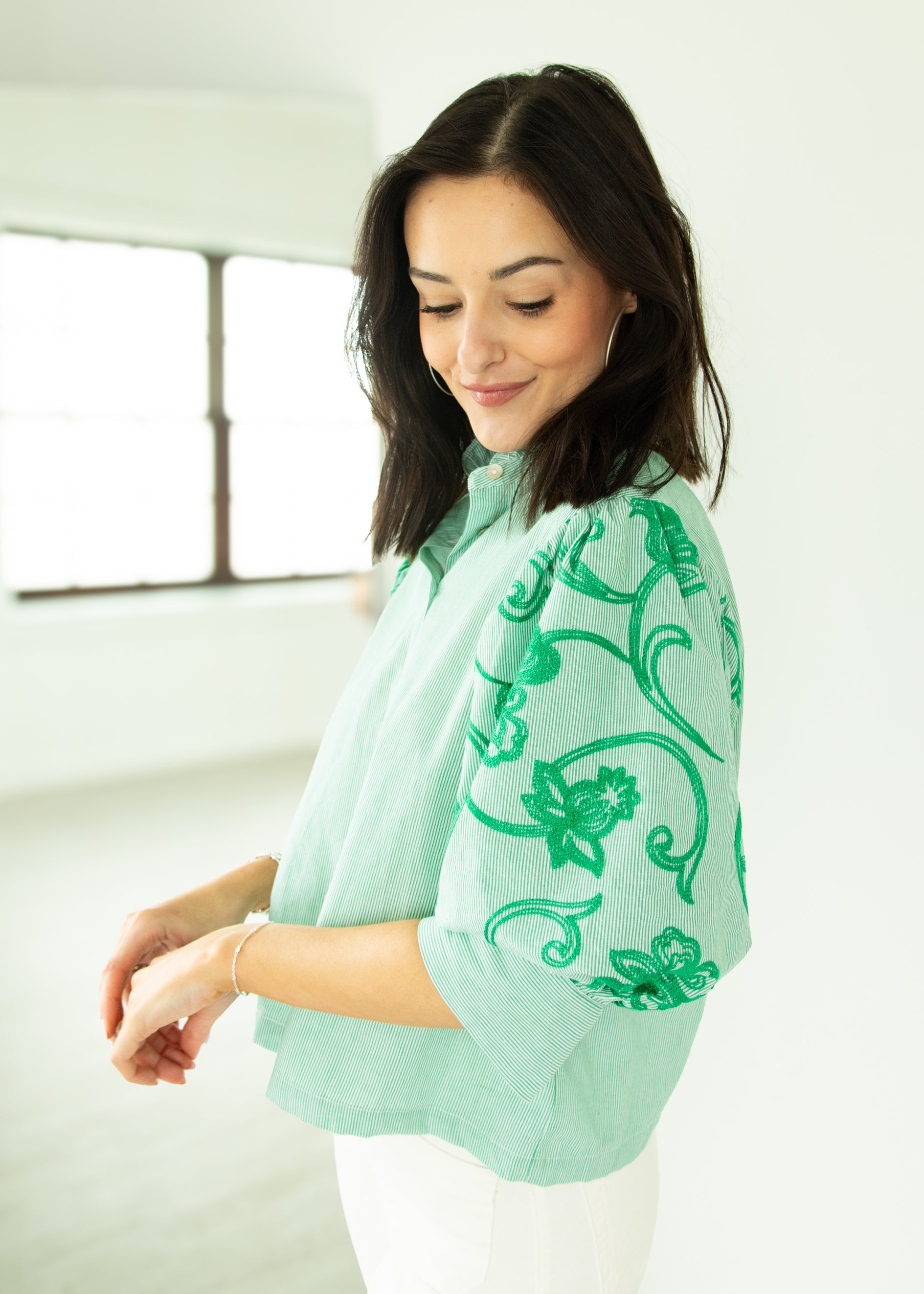 Woman wearing a light green blouse with floral patterns in a minimal indoor setting