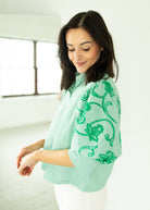 Woman wearing a light green blouse with floral patterns in a minimal indoor setting