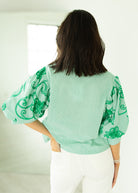 Person wearing a light green blouse with green patterns in a minimal indoor setting