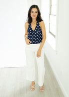 Woman wearing a navy polka dot top and white pants in a bright room.