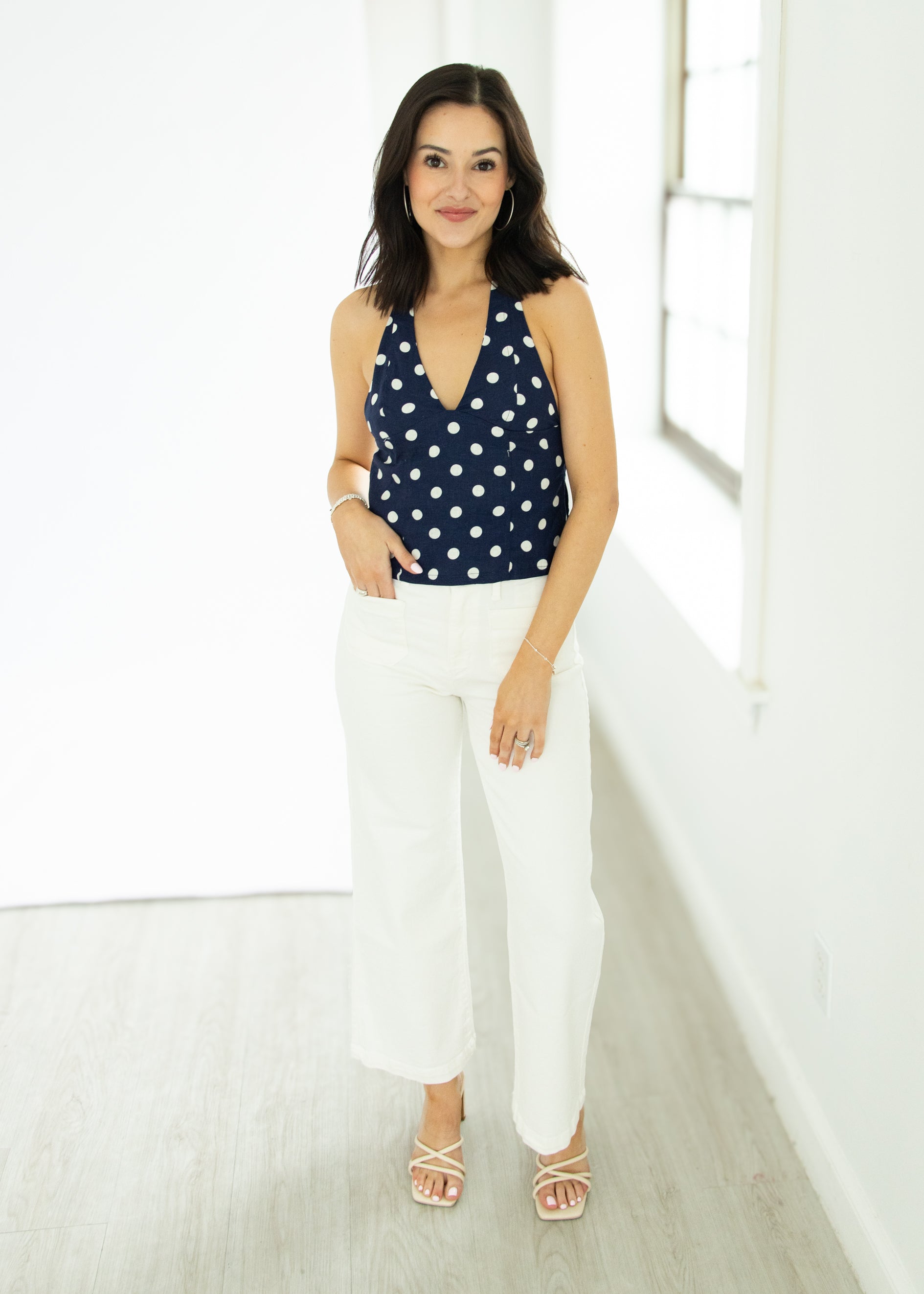 Woman wearing a navy polka dot top and white pants in a bright room.